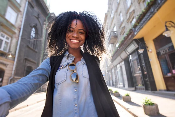 Привлекательная молодая черная женщина позирует перед камерой с сияющей улыбкой и вьющимися волосами . — стоковое фото