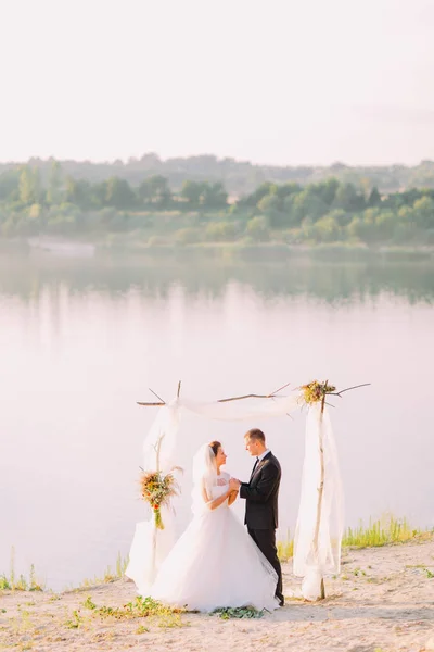 De volledige weergave van het bedrijf handen jonggehuwden tijdens de ceremonie van het huwelijk in de buurt van de rivier. — Stockfoto