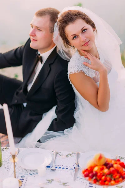 De close-up portret van de bruid zit back-to-back aan de bruidegom achter de bruiloft picknick. — Stockfoto