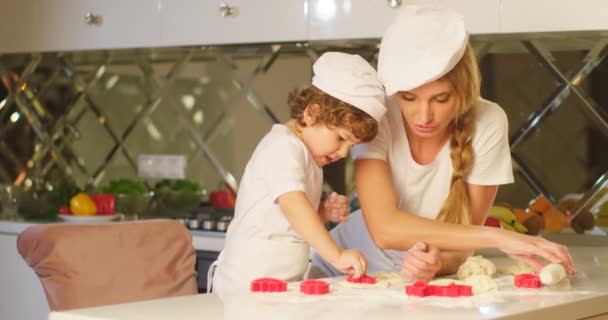 Krásné kompozice krásné matky učí svého syna, jak hníst těsto, použijte soubor cookie formičky na moderní kuchyni. — Stock video