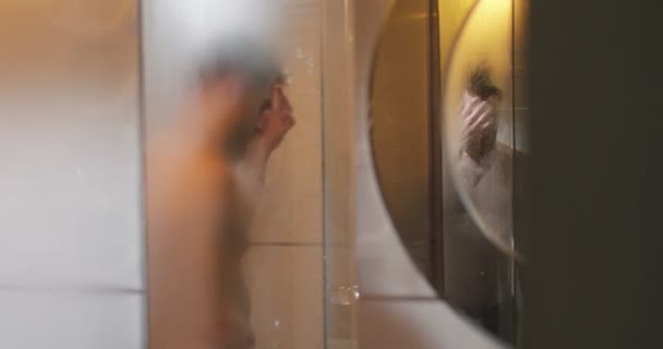 La vue arrière de l'homme déprimé sous la douche. Le reflet dans le miroir . — Video