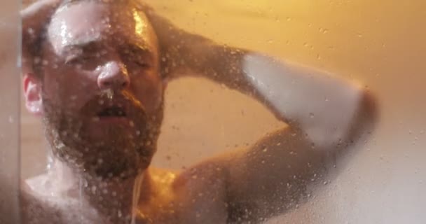 L'uomo allegro sta lavando i capelli sotto la doccia. La vista ravvicinata attraverso la doccia vasca da bagno in vetro . — Video Stock