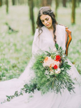 Onun clourful buket düğün ve yeşil ahşap sandalye üzerinde oturan bakarak kahverengi saçlı güzel gelin.