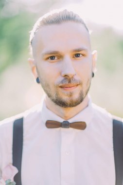 Burun piercing ve ahşap kelebek yeşil alanda damat yakın çekim portresi.