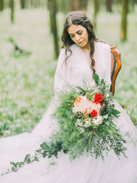 Onun clourful buket düğün ve yeşil ahşap sandalye üzerinde oturan bakarak kahverengi saçlı güzel gelin.