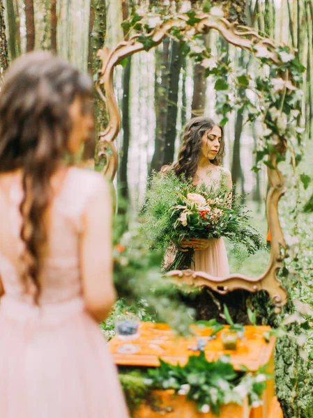 La foto de la mujer con el pelo largo y rizado y un enorme ramo de colores mirando al lado derecho y su fermentación en el espejo. La foto de cerca en el bosque . — Foto de Stock