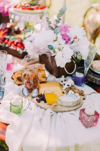 Η ρύθμιση του πίνακα γάμου. Υπάρχει μια ξύλινη σανίδα γεμάτη από διάφορα είδη τυριών και τοποθετείται κοντά στο γλάστρες, υπέροχο κέικ και κεριά. — Φωτογραφία Αρχείου