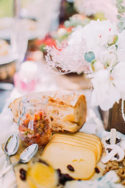 A deliciosa composição do queijo, pão e cogumelos cercados por flores nas panelas de madeira . — Fotografia de Stock