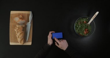 Salata ve kesilmiş ekmek yakınında bir telefon tutarak ellerinde Üstten Görünüm.