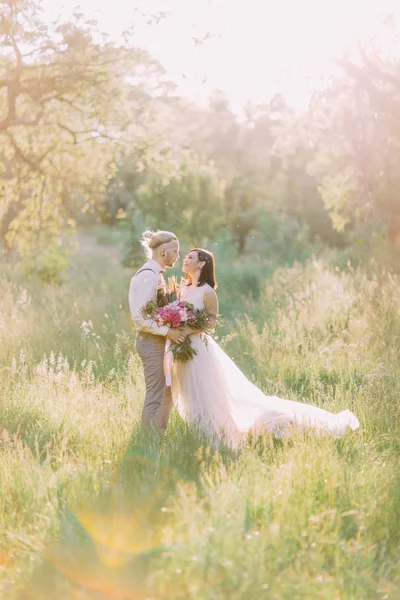 Das schöne vertikale Foto des frisch vermählten Paares, das sich im Hintergrund des sonnigen Feldes hält. — Stockfoto