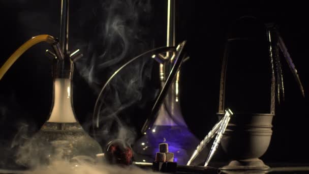 Creative dark composition consisting of hookahs and smoke equipments wrapped by the huge cloud of smoke. The hookah is changing the colours. — Stock Video