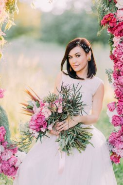Gelinle peonies buket düğün çiçek arch adlı arka plan bahar ormanın içinde oturuyor. Yakın çekim portre.