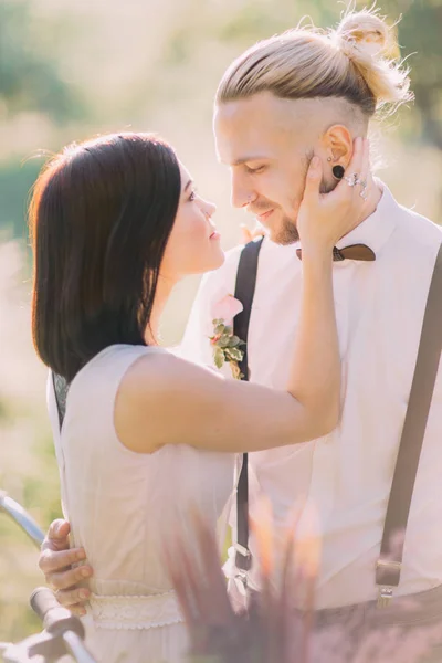 El retrato de cerca de la novia en el vestido de novia blanco acariciando al novio vestido moderno en el bosque soleado de primavera . —  Fotos de Stock