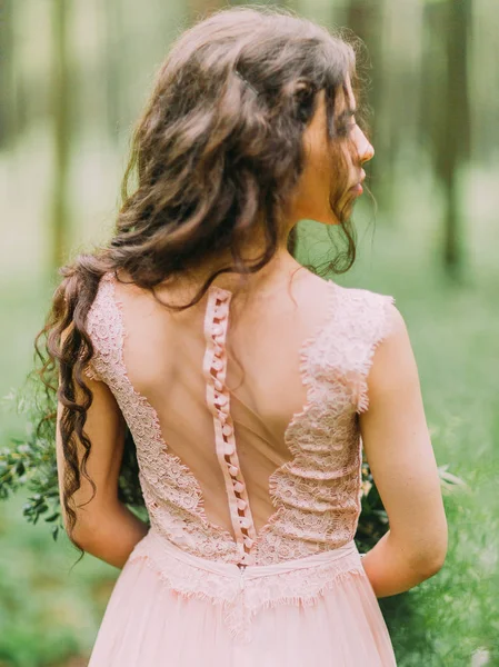 La espalda desnuda decorada con encaje de la mujer con el pelo largo rizado en vestido rosa. Foto de cerca en el bosque verde . — Foto de Stock