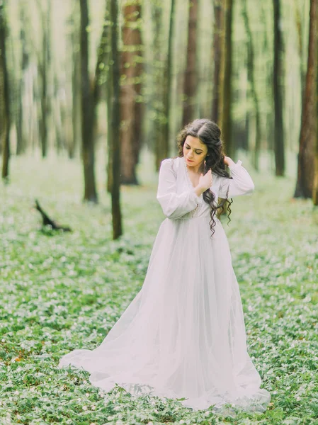 Il ritratto ravvicinato della bella donna con l'abito da sposa bianco che guarda il terreno e ordina i capelli nella foresta verde . — Foto Stock