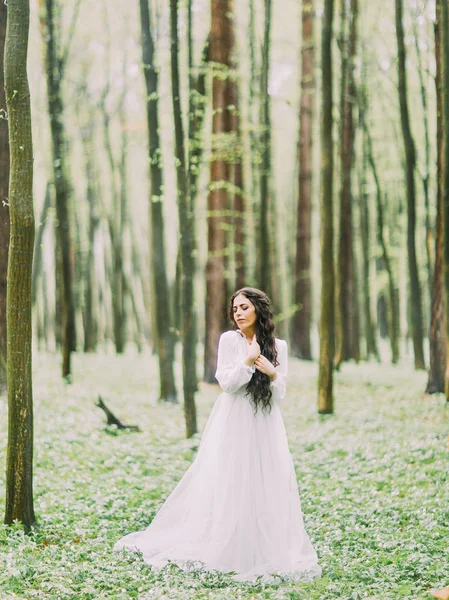 Full-hög porträttet av bruden med brunt hår i lång vit brudklänning tittar till höger i den gröna skogen. — Stockfoto