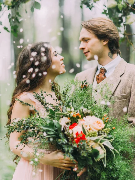 Närbild sida ståenden av de härliga nygifta ser in i varandras ögon och bruden håller stor färgstark bukett. — Stockfoto