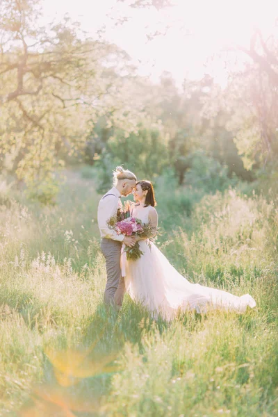 Portrait mignon de la mariée dans la longue robe blanche tenant le bouquet rose tandis que le meilleur homme la caresse . — Photo
