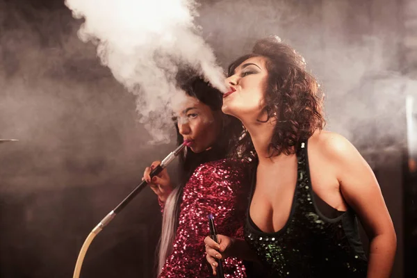 Сексуальные девушки выдыхают кальяновый дым изо рта. Женщины с ярким макияжем и красивыми прическами . — стоковое фото