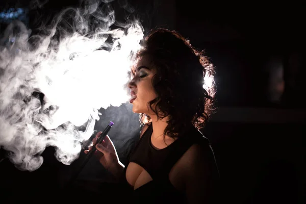 Mujer bastante rizada exhala una nube de humo después de fumar narguile . — Foto de Stock