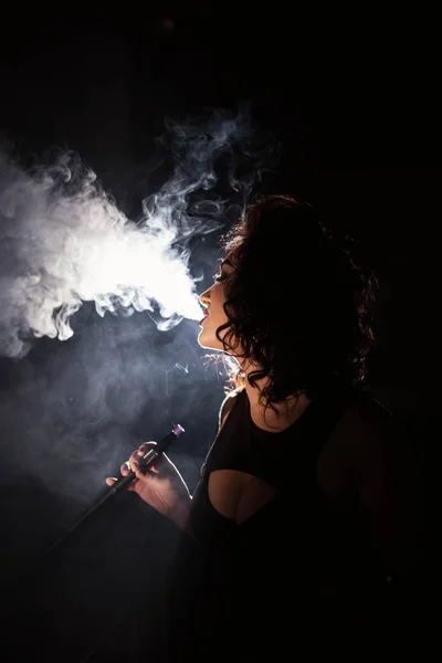 Retrato de mulher muito encaracolada exalando fumaça em um fundo escuro . — Fotografia de Stock