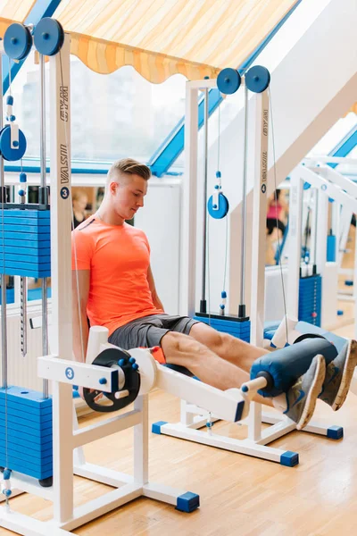 Oldalon a fénykép egy fiatal srác az edzőteremben képzés láb nyomja meg, hogy meghatározzák a felső lábszár izmait. — Stock Fotó
