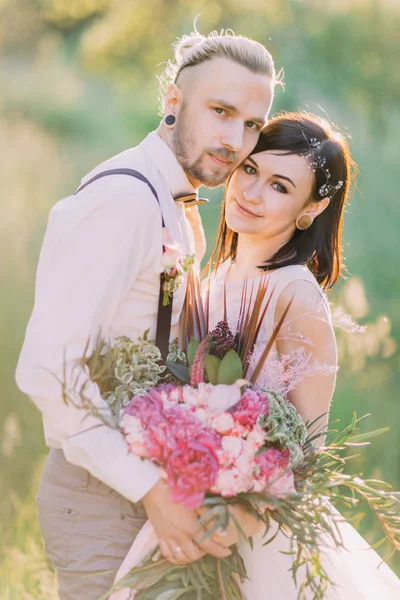 Braut mit den Haarschmuck-Accessoires und Bräutigam im modernen Kleid halten und umarmen sich im Wald. — Stockfoto