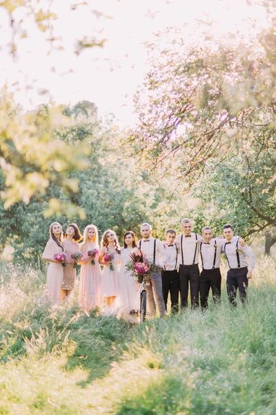 The full-hight photos of the newlywed couple, best men and bridesmaids holding the bouquets of the pink flowers in the forest. — Stock Photo, Image