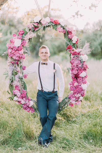 Modern mavi elbiseli sarışın en iyi adam düğün peonies arch adlı güneşli ahşap arka plan üzerinde oturuyor.