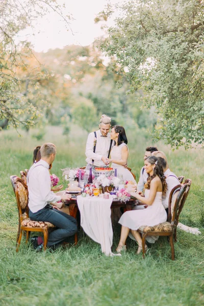 Foto av nygifta skära sin första bit av bröllopstårta tillsammans, medan gästerna tittar på den. Skogens sammansättning. — Stockfoto