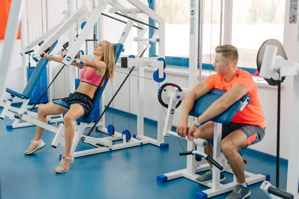 Hübsche Frau, die im Fitnessstudio trainiert. macht Übungen für Arme. perfekte Körper. Mann schaut sich das Mädchentraining an — Stockfoto