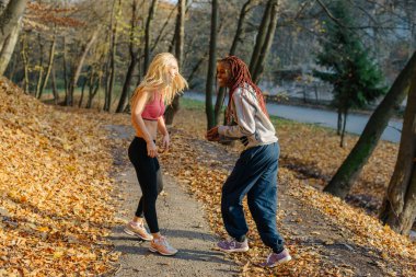 Kızlar autamn Park'ta jogging sonra eğleniyor. Gülümseyen kadın sarışın ve Afrika