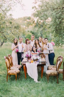 Mutlu yeni evliler gülümseyen onların nedime ise düğün masada oturan ve en iyi erkek arkalarında güzel yeşil ahşap arka plan ayakta duruyorlar.