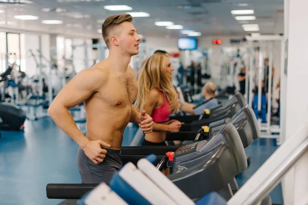 Fiatal férfi és női futó futópadok edzőteremben. Fickó csupasz test. — Stock Fotó