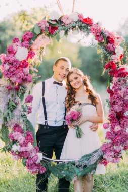 Yakın çekim portre çiçekler ve en iyi adam içinde belgili tanımlık karanlık ile güzel nedime uygun pembe çiçeklerden yapılmış büyük düğün kemerin arkasında sarılma.