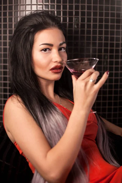 Çekici kız bir barda oturmuş ve kamera için poz onun elinde camlı.