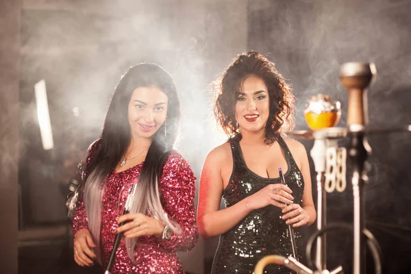 Genç kadınlar güzel elbiseler ve nargile borular onların elinde tutan ve gülümseyen güzel saç modelleri.