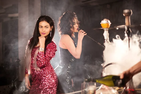 İki esmer kısa parlak elbiseler, nargile bar veya bir restoran kamera için poz.