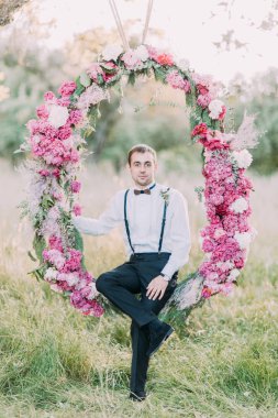 Güneşli parkta bulunan peonies kemer üzerinde oturan en iyi adam tam-yüksekliği portresi.