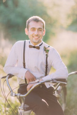 Siyah takım elbiseli en iyi adam gülümseyen güneşli park arka plan, becycle oturuyor.