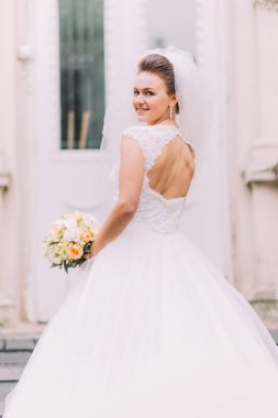 Sarı buket tutarak ve kameraya bakarak gülümseyen gelini arkasında çıplak.