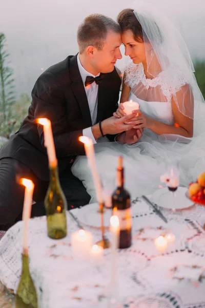 De vrolijke pasgetrouwden zitten met kaarsen van head-to-head zijn tijdens hun picknick. — Stockfoto