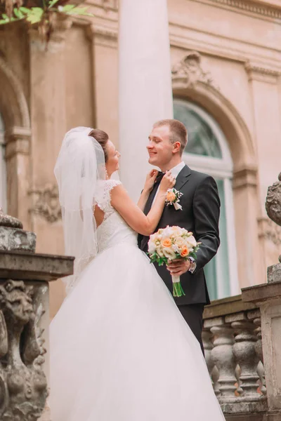La novia está corrigiendo la pajarita del novio que sostiene el ramo de bodas . —  Fotos de Stock