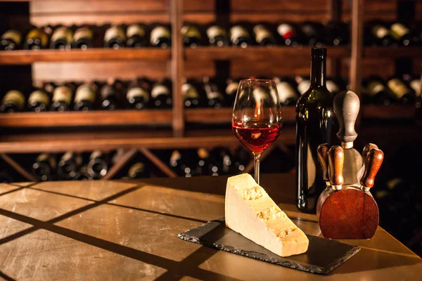 Bicchiere di vino, formaggio e accessori su un tavolo di legno in una volta di vino . — Foto Stock