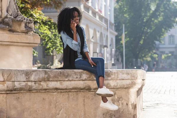 Cep telefonu aracılığıyla konuşurken havuzun üzerinde oturan muhteşem Afro-Amerikan kız yatay görünüm.