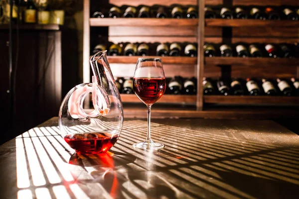 Carafe de vin et verre de vin sur un fond d'étagères à vin . — Photo