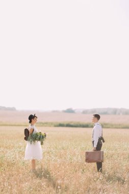 Uzak duran alanında yeni evliler tam uzunlukta dikey yan fotoğraf. Gelin Damat vintage çanta taşıyor ise renkli buket tutuyor.
