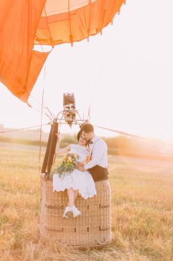Vintage giyinmiş gülümseyen yeni evliler airballoon sepete oturuyorsun ve buket gelinle damat üzerinde yaslanmış. Alan kompozisyon
