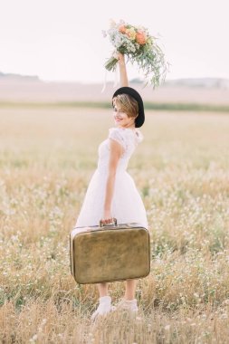 Vintage çanta taşıyan, renkli buket kadar tutmak ve güneşli alan arka kameraya bakarak gülümseyen gelini yan görünüm.