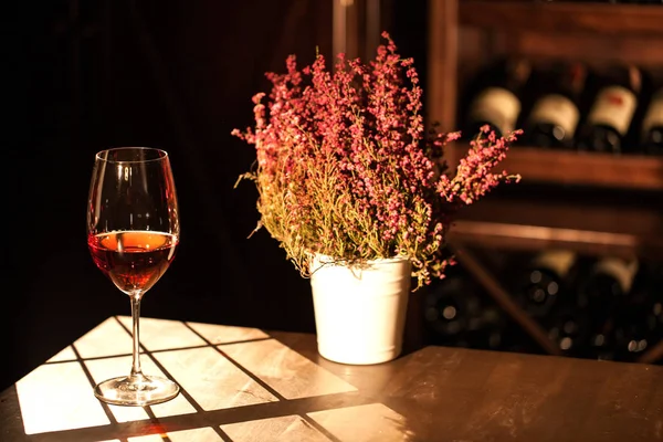 Composizione romantica orizzontale del bicchiere di vino e vaso di fiori posto sul tavolo nella cantina . — Foto Stock